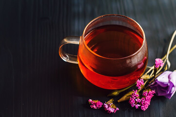 black tea in a transparent Cup next to a purple flower on a dark wooden background