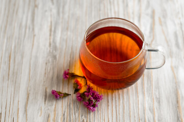 black tea in a transparent Cup next to a purple flower on a light wooden background