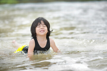Cute Asian child swimming at the sea.Little boy having fun under the sun and in the water.Outdoor activity for preschooler.Joy.Sports in outdoors.Playful young male in the beach waves.
