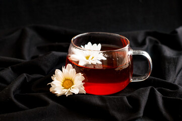 black tea in a transparent Cup with chamomile on a dark background