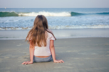 Fototapeta na wymiar young girl sit on sand and looking at water