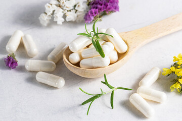 Fototapeta na wymiar Collagen capsules for skin and beauty in the wooden spoon with herbs and flowers on white marble table close up. Health care concept.