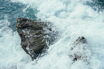 Big stones in azure water of mountain river close-up. Blue nature background with big boulders in turquoise water of mountain creek. Full frame of sea surf. Ocean surf among stones. Backdrop of tide.