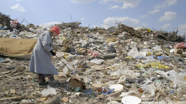 homeless woman seeking for used things and food in city dump among waste. Poverty, social problem, unemployment.
