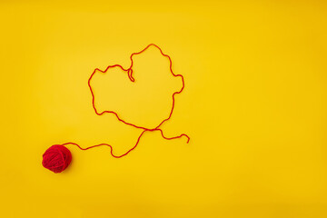 the heart of a red woolen thread from a ball is on a yellow background