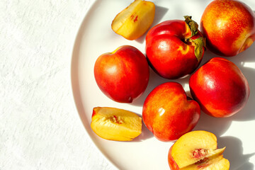 Red ripe organic nectarine fruits on the white plate on nature background. Summertime healthy eating concept. Fruit antioxidant. Selective focus. Top view. Space for text