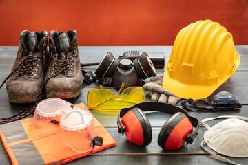 Work safety protection equipment. Industrial protective gear on wooden table, red color background.