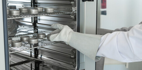 A gloved lab technician removes hot sample bottles from the drying chamber. - obrazy, fototapety, plakaty