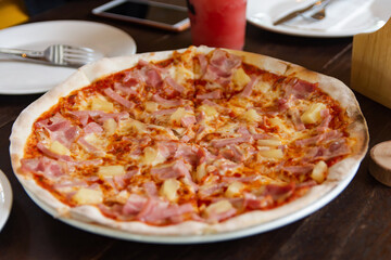 hawaiian pizza with ham, pepperoni, tomatoes on wooden table