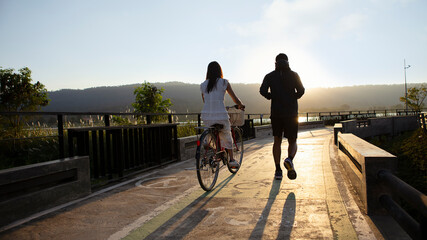 A young woman cycling with her boyfriend running for exercise 16:9