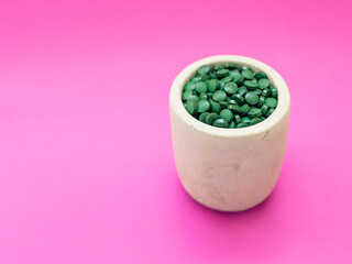 Obraz na płótnie Canvas Green hawaiian spirulina in tablespoons pills on pink background. Super food, healthy lifestyle, healthy supplements concept