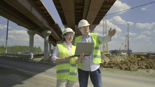 man and woman working on background of construction overpass. Builders discussing future work plan for erection of bridge using computer.