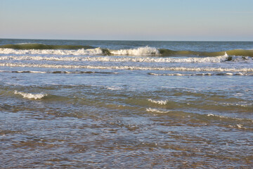 The shore of the sea at low tide, visible sea waves in the distance.