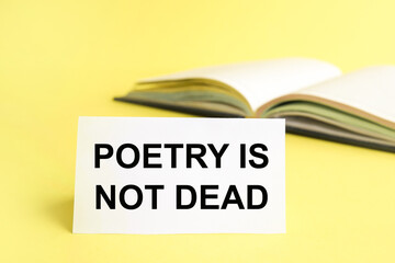 Text sign showing Poetry Is Not Dead. Conceptual photo aesthetic and rhythmic writing is still alive and modern. Text on white paper on a yellow background near the diary