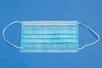 The medical mask lies on a blue background. Protection from viral diseases.