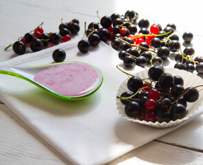 Fresh black and red currant with green leaves on white wooden boards. Homemade yogurt with berries  in spoon.