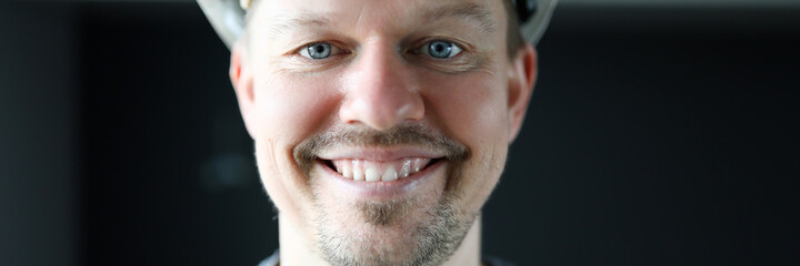 Obraz premium Happy builder man in helmet stands in apartment. Man is standing in room and smiling. Work is performed by qualified specialist. Highest level security and performance. Successful repairman service