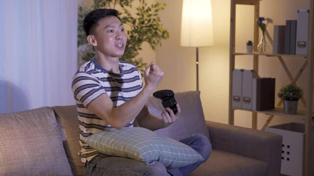 leisure activity asian man feeling happy with victory and laughs at his opponent, giving him the finger. Overjoyed young guy cheers for triumph talking smack and making offensive gesture to enemy.