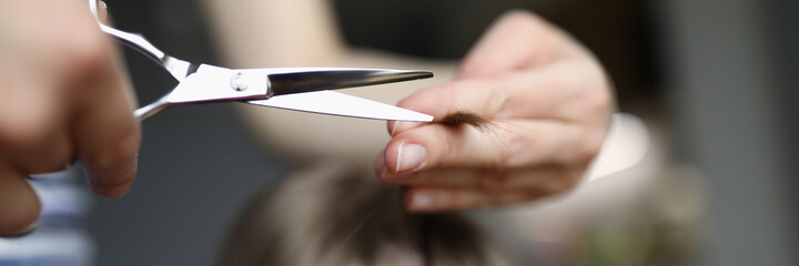 Mom cuts baby hair with scissors at home, hairstyle. Woman does hairstyle for child at home during quarantine. Hairdresser works on visit to clients house. Hair trendy stylist training