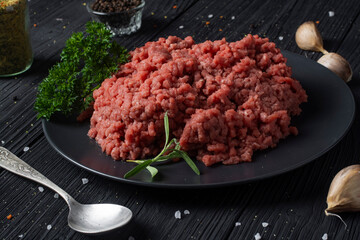 Black plate with minced meat on a black wooden table.