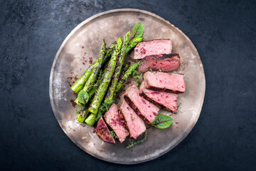 Barbecue dry aged wagyu roast beef steak with green asparagus and lettuce offered as top view on a...