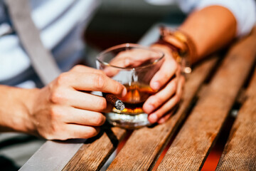 a glass of whiskey and a cigar in men's hands, men's hands on the table, a man sitting at a table in a cafe on the street