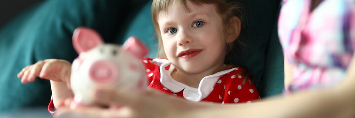 Mom and daughter sit home on couch with piggy bank. Child is able to plan future for years to come. Child learned to do simple mathematical calculations. Learn to plan financially correctly