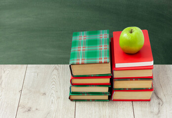 Back to school, pile of books in colorful covers and green apple on wooden table with empty green school board background. Distance home education. Quarantine concept of stay home.