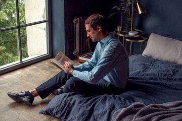 young man reading a book, a guy in a blue shirt in the interior of a stylish apartment