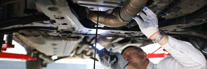 Close-up of professional car mechanic with assistant changing motor oil in automobile engine at...