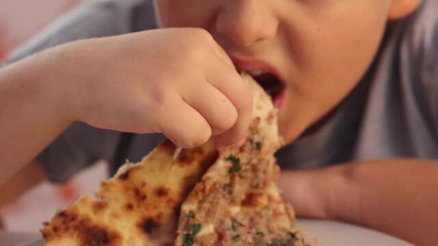 Boy hungrily bites and chews rolled Turkish pizza lahmacun. High quality FullHD footage