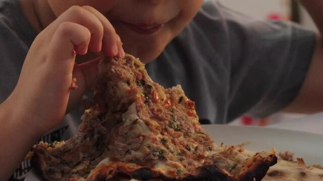 Boy hungrily bites and chews rolled Turkish pizza lahmacun. High quality FullHD footage