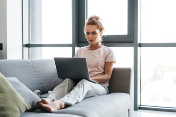 Naklejka premium Image of focused woman working with laptop while sitting on couch