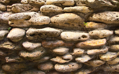 Wall made of round stone, beige-yellow color. Old fence of masonry. Sea stones of different sizes, stacked.