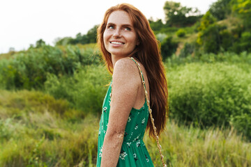 Naklejka na ściany i meble Beautiful smiling girl wearing summer dress walking in a meadow during sunset