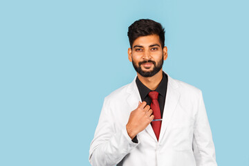 Handsome modern indian / asian doctor with stethoscope, tie and white coat on blue background