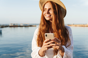 Image of joyful woman using mobile phone while walking on promenade