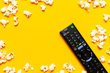 Black TV remote control and popcorn on bright yellow background flat lay top view copy space....