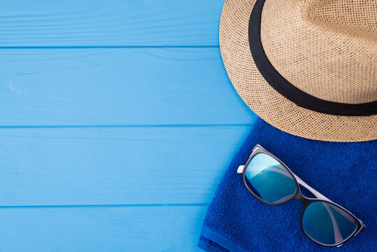 Summertime vacation concept. Top above overhead view close-up photo of a towel sunglasses and a sunhat isolated on blue wooden background with copyspace
