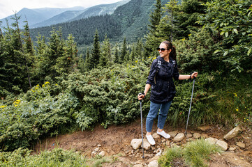 Female hiker with a sticks for a nordic walking in the mountains. A girl with a backpack on the mountain footpath