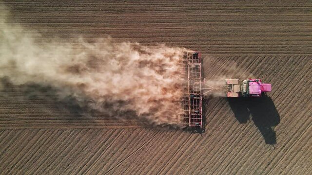 Shooting from drone flying high over tractor with harrow system plowing the ground on cultivated farm field, preparing soil for planting new crop next season, agriculture concept, top view.