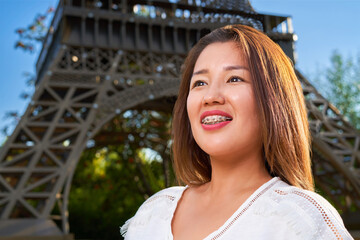 Girl of Asian appearance in a white T-shirt with braces, looks to the side and smiles, blurred background