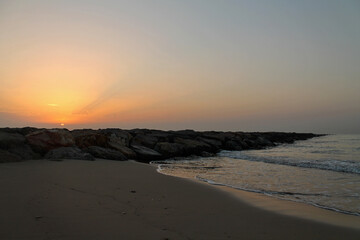 A beautiful and relaxing sunrise on the beach. Orange sky illuminates the breakwater