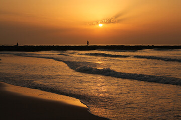 unrecognizable people enjoying a beautiful sunrise on the breakwater of the beach. Men relax watching the orange sky as the sunrises