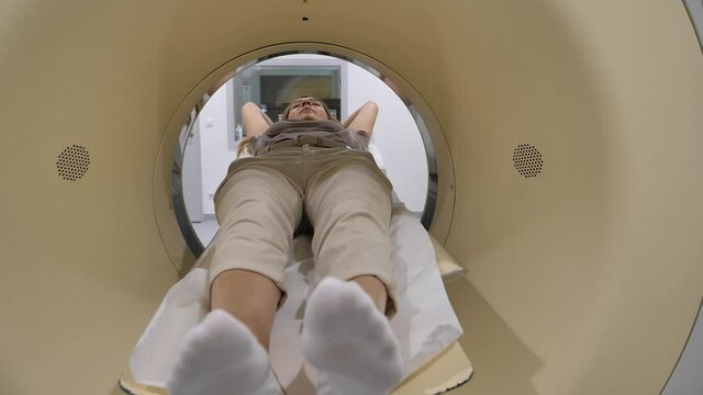 40-50 years old woman enters a CT scanner for examination at a hospital. Selective focus on the patient head in the foreground.