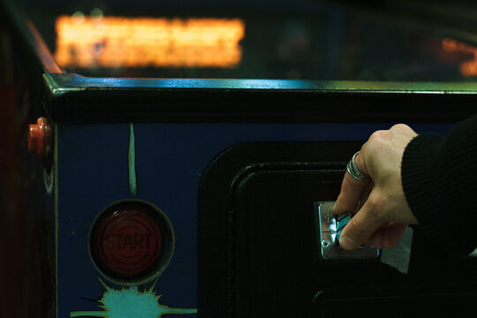 Close up of a woman inserting coin in pinball machine
