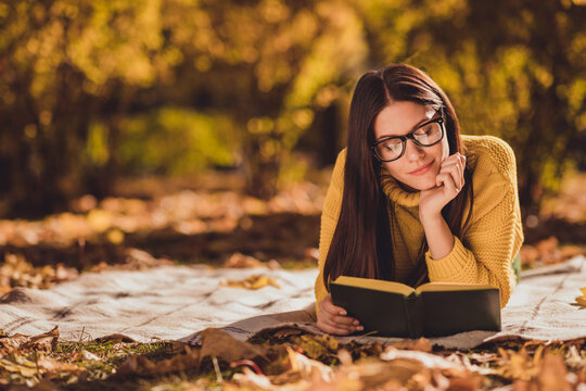 Photo of positive girl rest relax in autumn forest park lawn lying checkered plaid blanket read interesting book wear yellow color pullover
