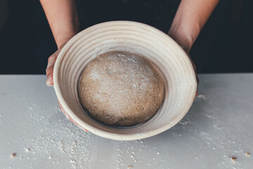 woman's hands holding a banneton with a bread dough