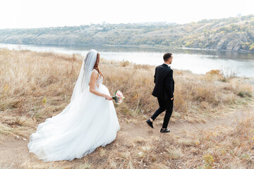 Wedding walk of a beautiful luxurious couple, the bride in a wedding white dress with a bouquet and the groom in a black suit in nature outdoors