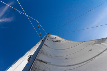 Bottom view of mast and sail of yacht on blue sky background, selective focus